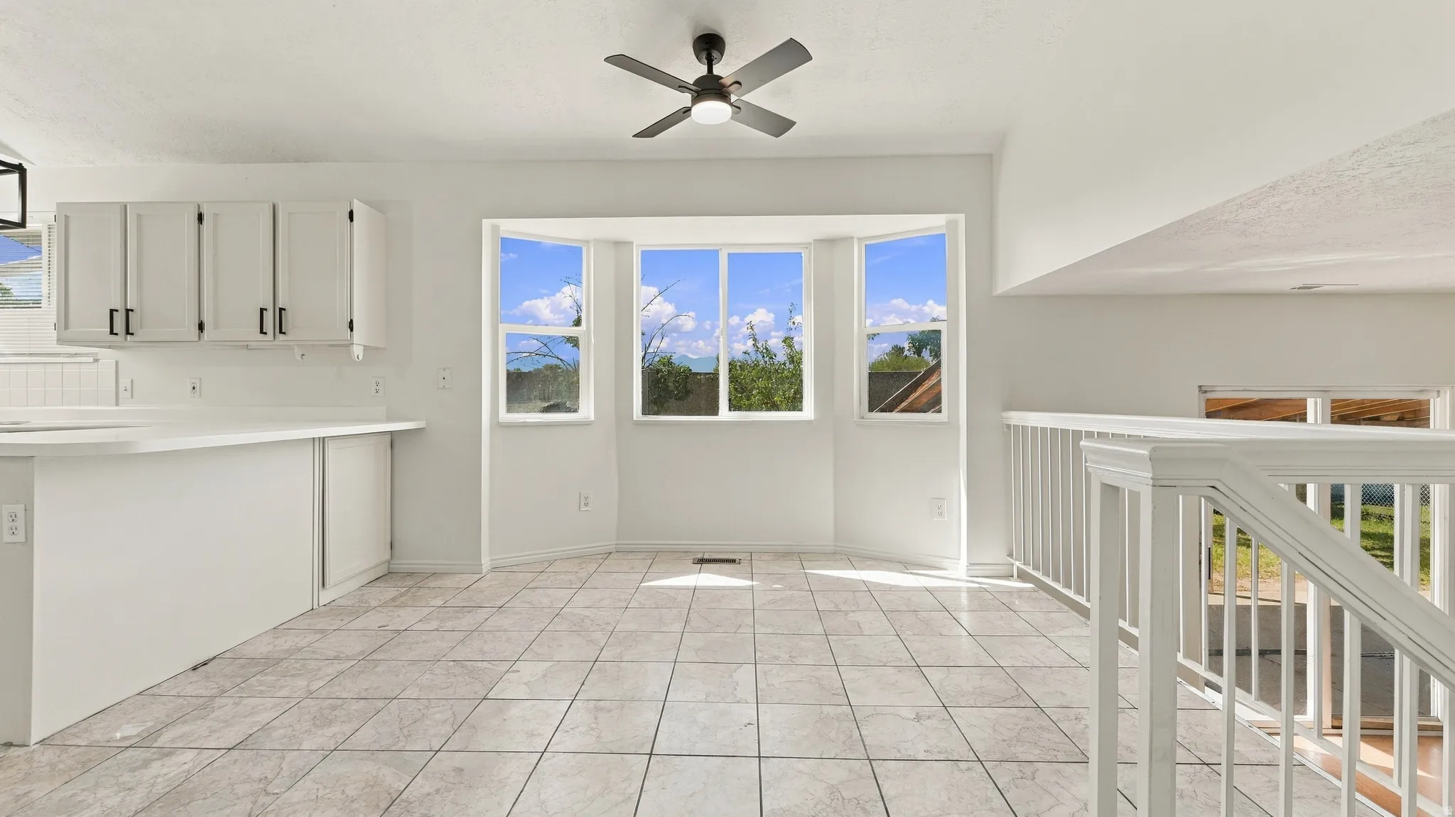 Spacious interior featuring a bay window, ceiling fan, white cabinetry, a kitchen island, and tiled flooring