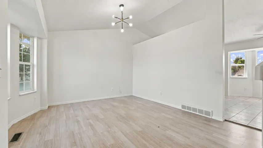 Vaulted ceilings, a contemporary light fixture, wood-finish flooring, and a bay window