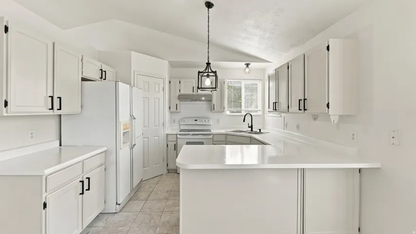 Kitchen featuring white cabinetry with black hardware, U-shaped countertops, ceiling-mounted light fixtures, and a vaulted ceiling
