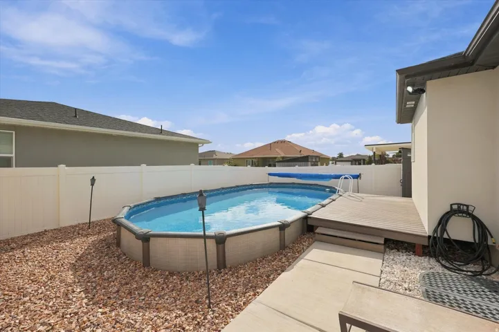 Above-ground swimming pool with an attached wood-finish deck, surrounded by gravel landscaping and a privacy fence