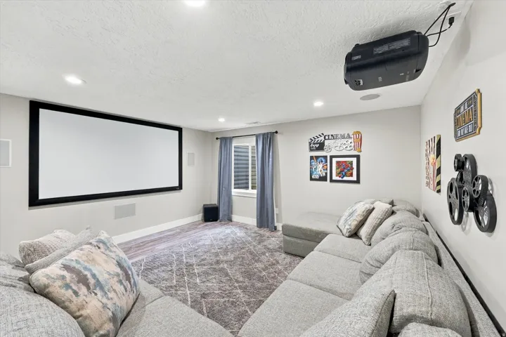 Dedicated media room featuring a large projection screen, mounted projector, recessed lighting, and wall-mounted speakers