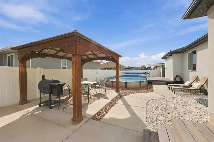 Outdoor living area featuring a wood-finish pergola, concrete patio, above-ground pool with surrounding deck, and decorative gravel landscaping