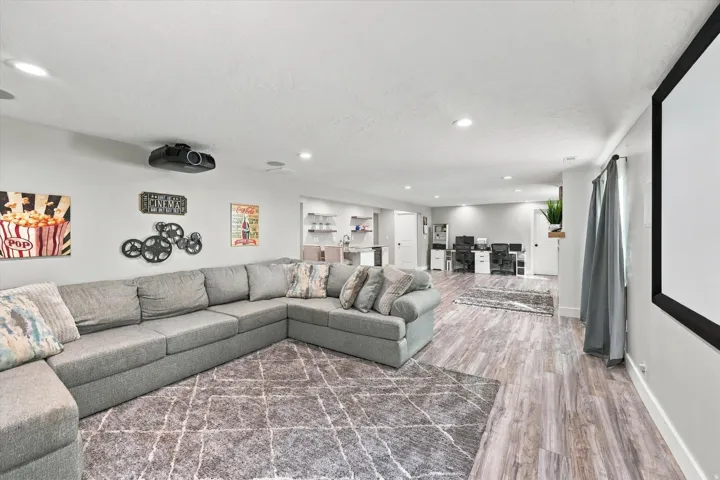 Recessed lighting throughout, wood-finish flooring, built-in projector, white baseboards, and a large screen