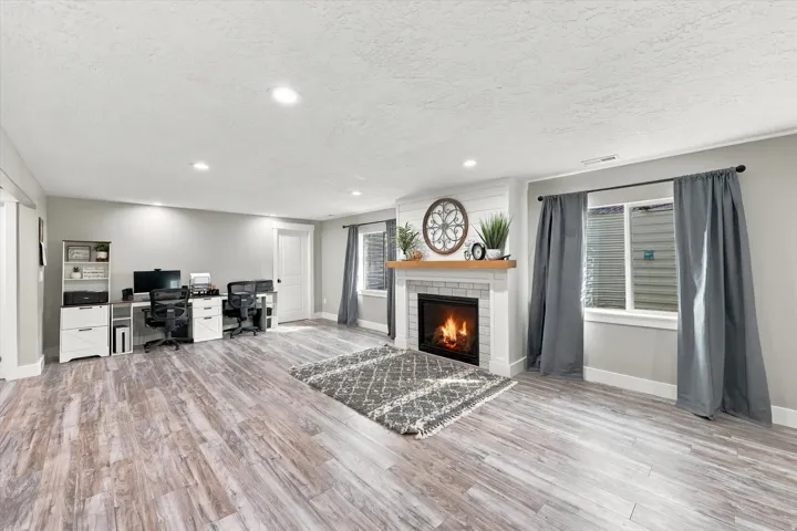 Spacious room featuring wood-finish flooring, recessed lighting, and a white brick fireplace with a wood mantle
