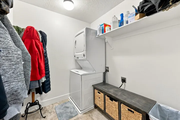 Laundry area featuring a stacked washer and dryer, an overhead shelf, a built-in bench, and light-toned flooring