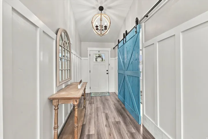 Vaulted ceiling with a decorative chandelier, white board and batten wall paneling, wood-finish flooring, and a blue barn door