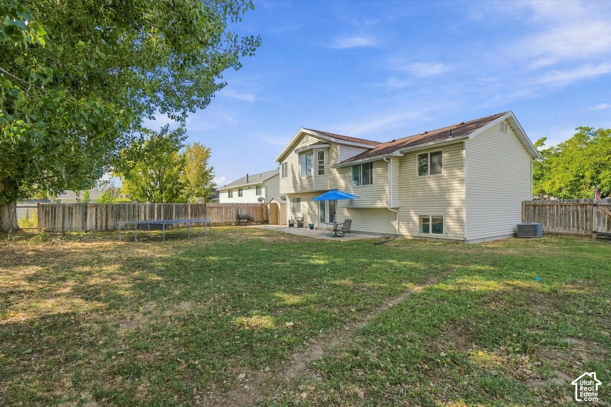 Spacious backyard featuring a wood fence, mature tree, and a ground-level patio