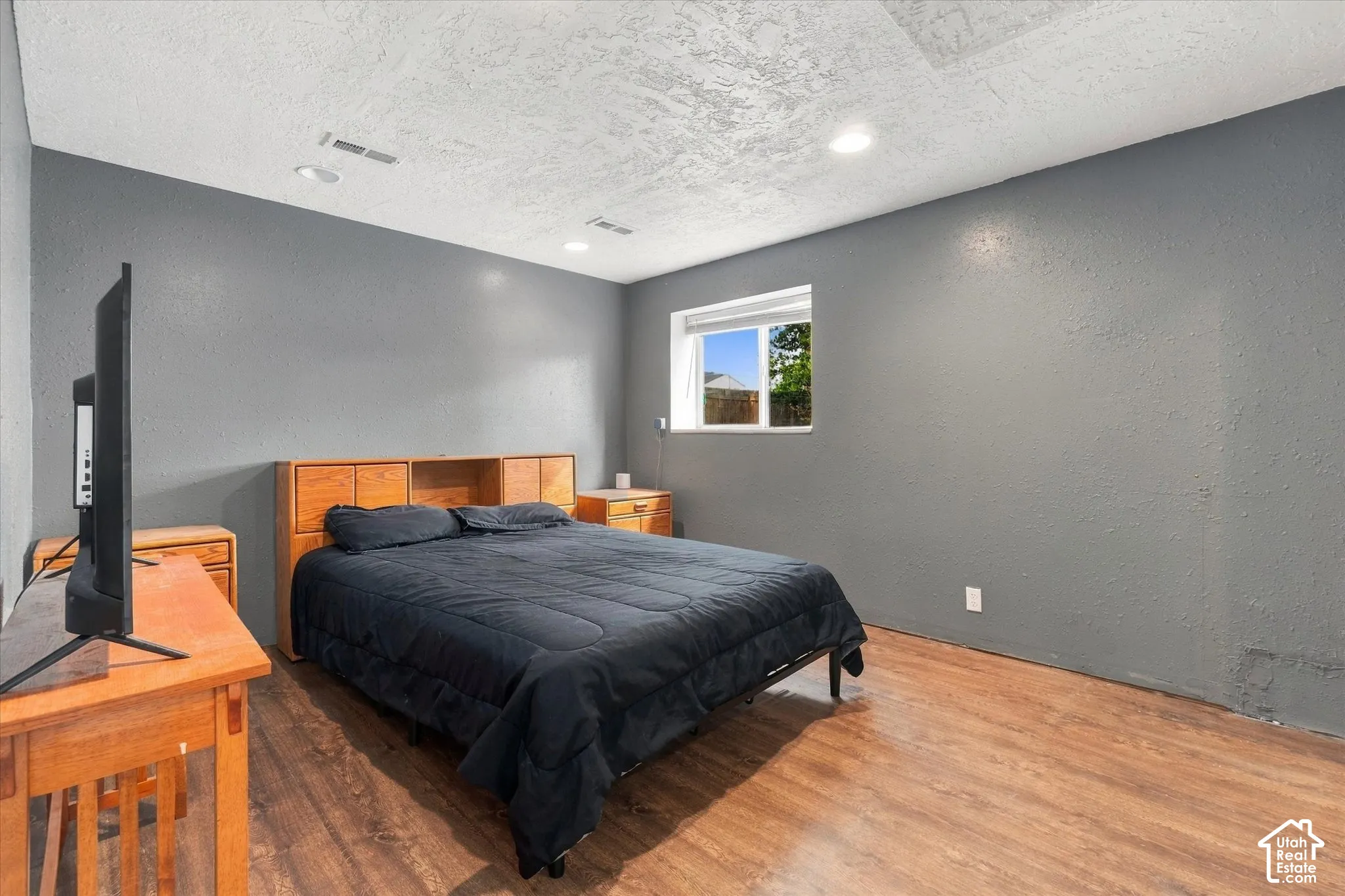 Wood-finish flooring with a textured gray wall, featuring recessed lighting and a window