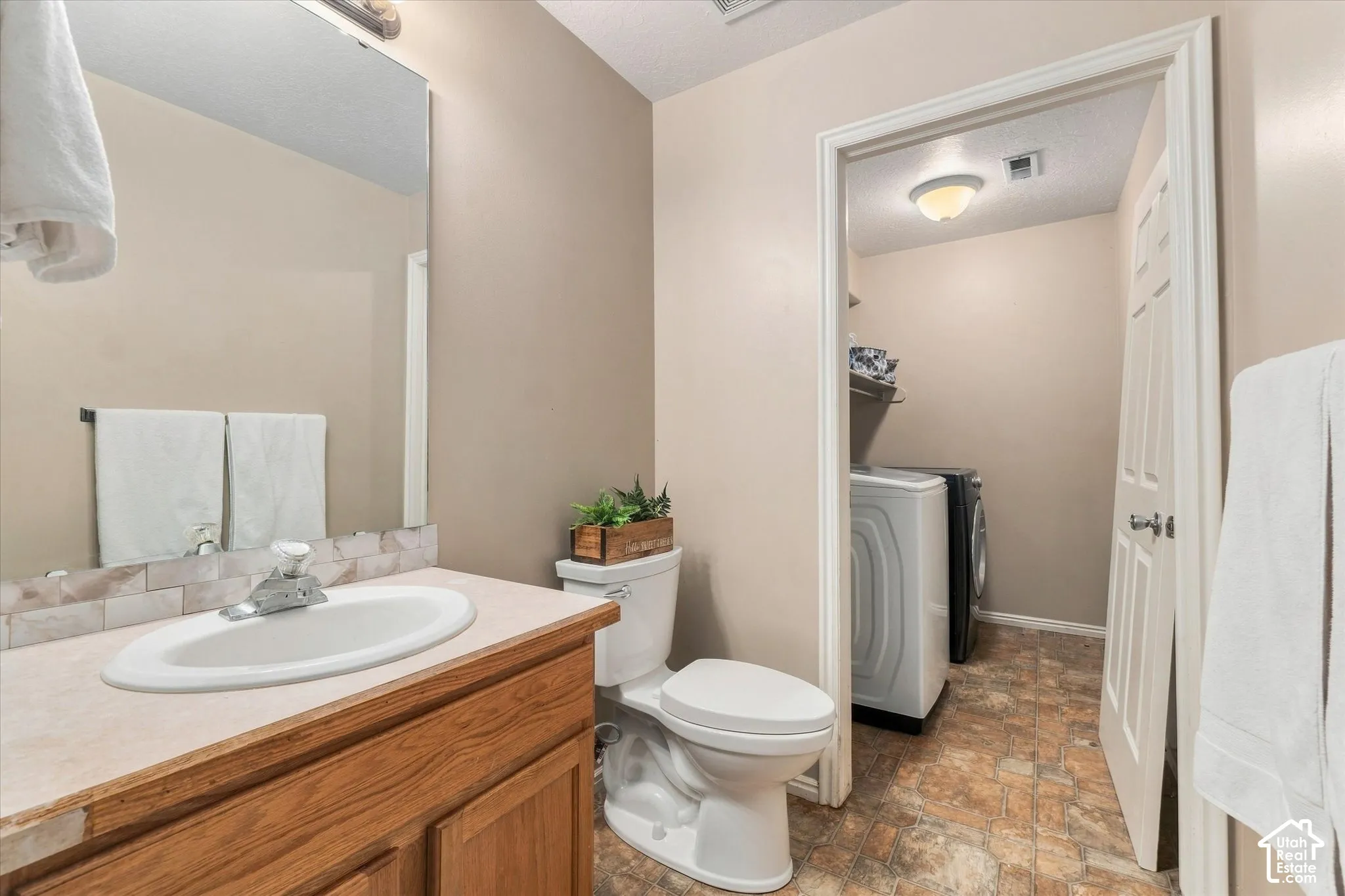 Bathroom featuring a wood-finish vanity with an integrated sink and a tiled backsplash