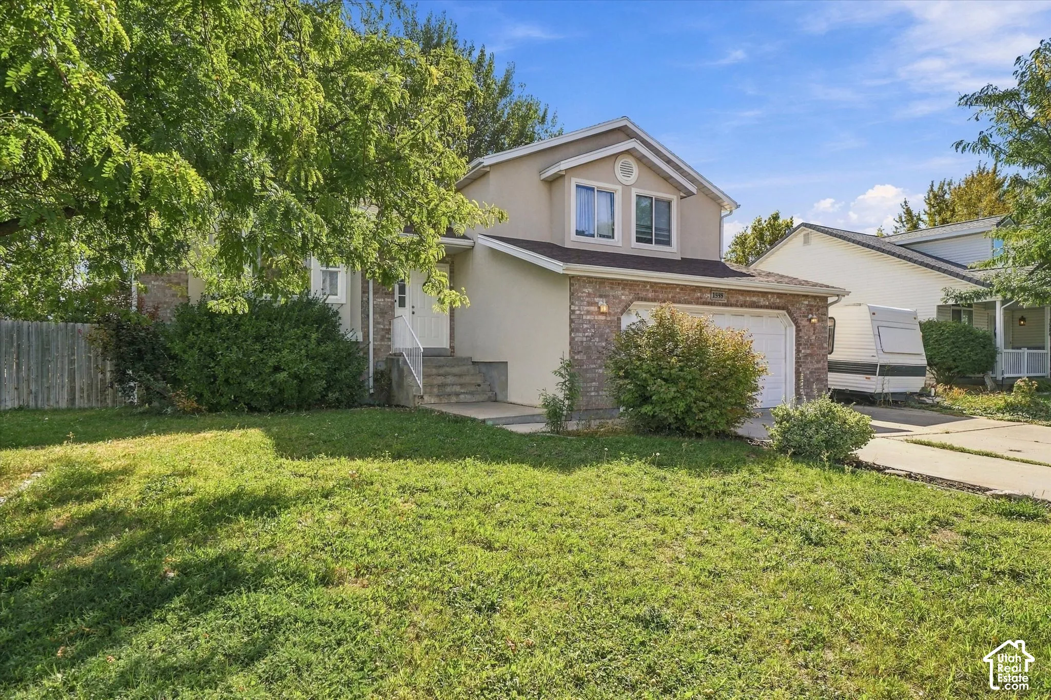 Two-story stucco and stone-finish exterior, attached garage, concrete driveway, and established front landscaping