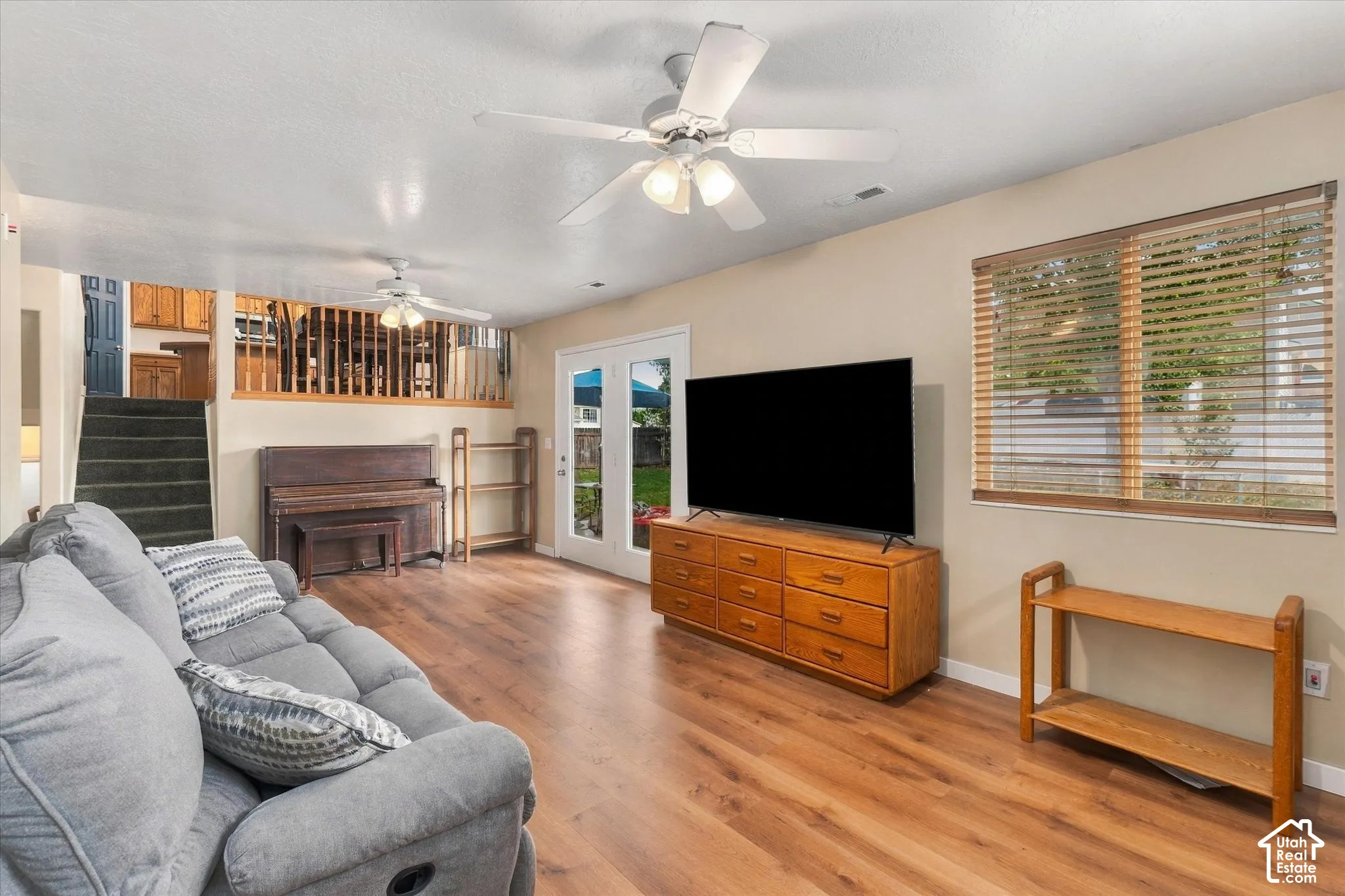 Wood-finish flooring, ceiling fan, natural light from exterior window, french doors, and staircase with carpeted treads