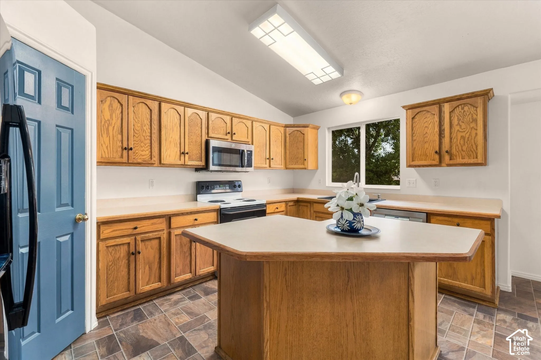 Kitchen featuring wood cabinetry, a center island with countertop, stainless steel microwave, and an electric range