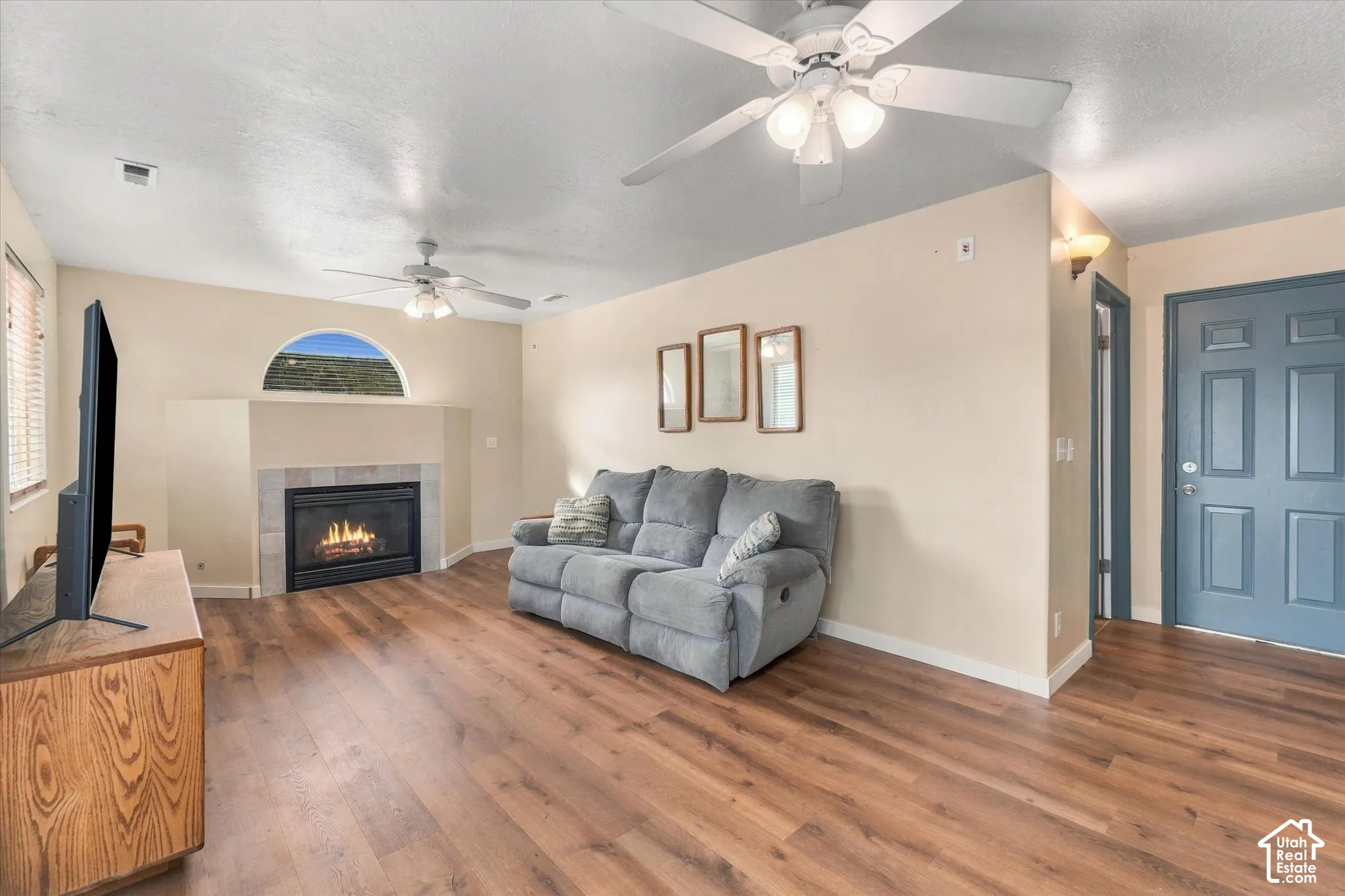 Spacious living area featuring wood-finish flooring, a fireplace with tile surround, and vaulted ceilings with ceiling fans