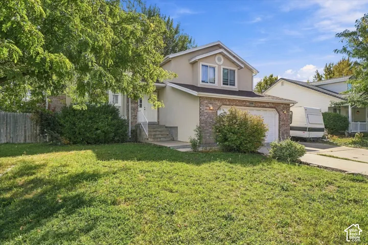 Two-story stucco and stone-finish exterior, attached garage, concrete driveway, and established front landscaping