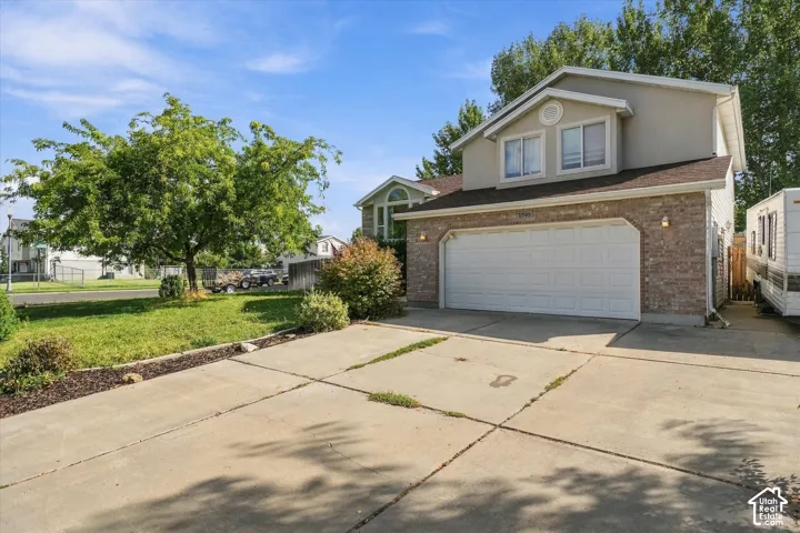 Two-story residence featuring a brick facade, attached two-car garage, concrete driveway, and a fenced side yard