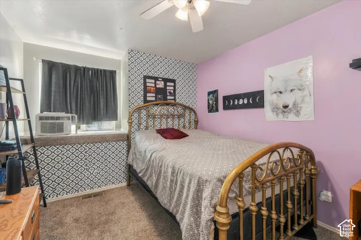 Carpeted flooring, patterned accent wall, ceiling fan with integrated lighting, and a window with a deep sill