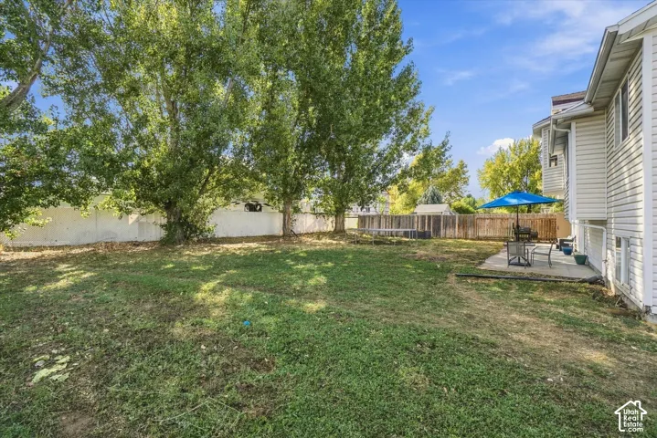 Expansive grassy yard with mature trees, a concrete patio, wood fencing, and white vinyl siding on the property