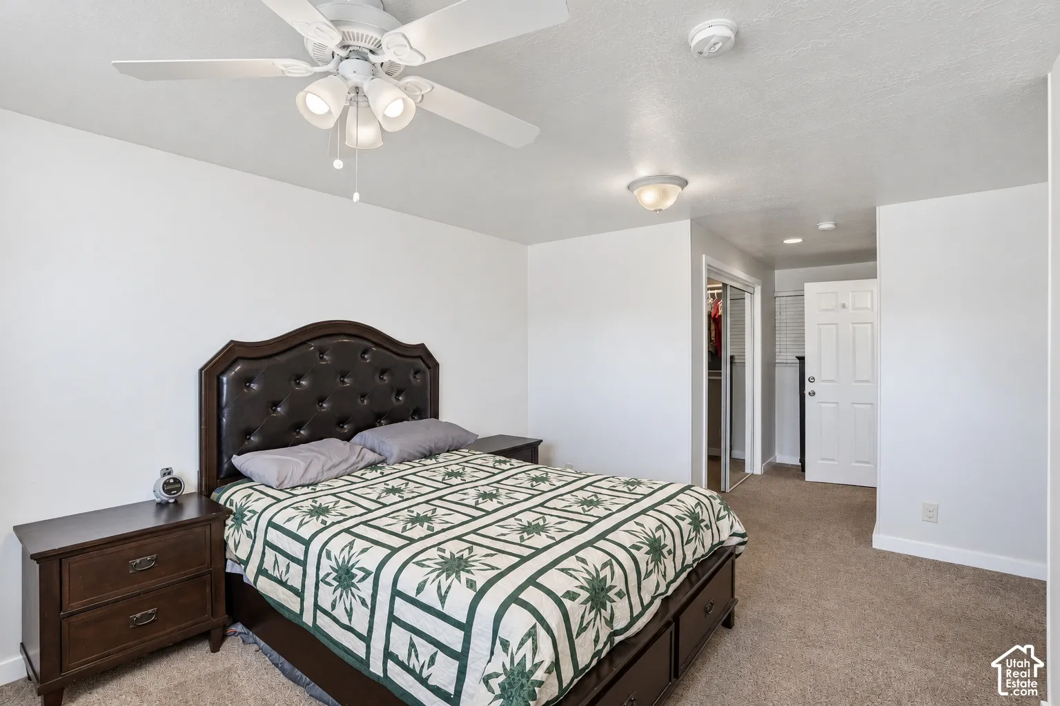 White walls with a ceiling fan light fixture, carpeted flooring, and a tufted headboard
