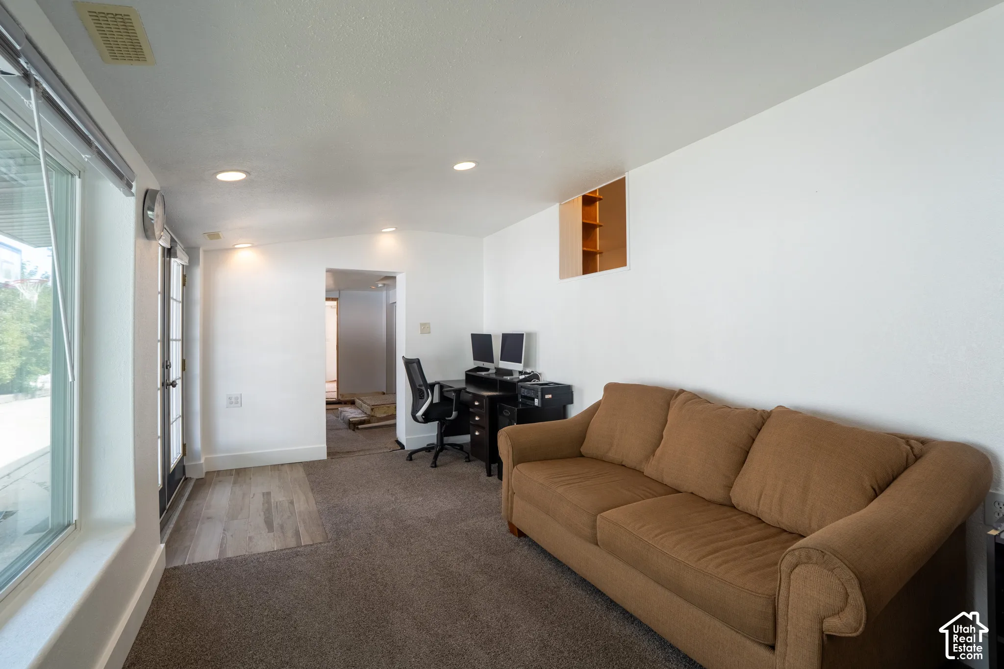 Recessed lighting illuminates an open space featuring a built-in shelving unit, dual French doors, and wood-finish flooring
