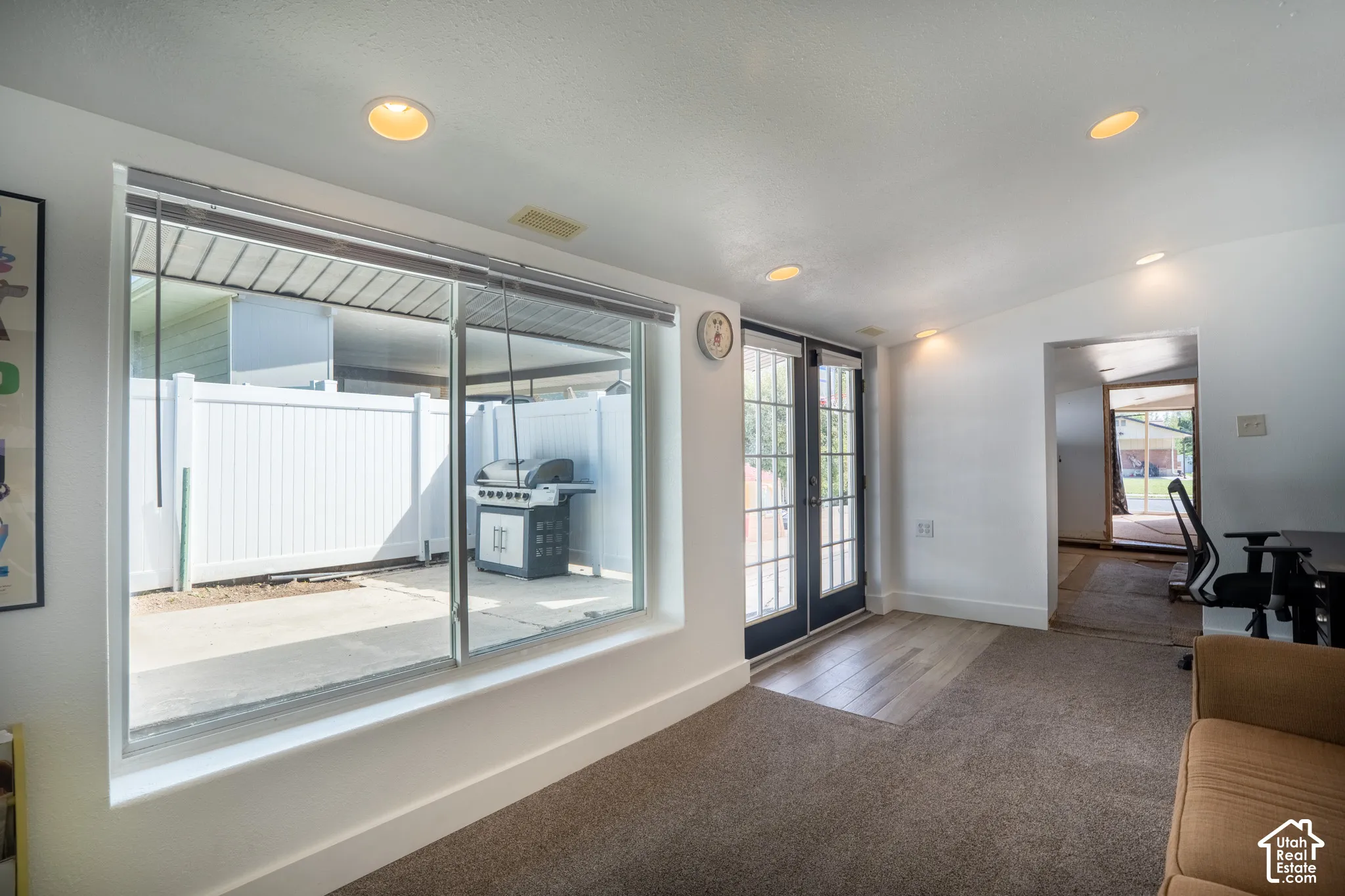 Recessed ceiling lighting, large picture window, white perimeter fencing, black French doors, and wood-finish flooring