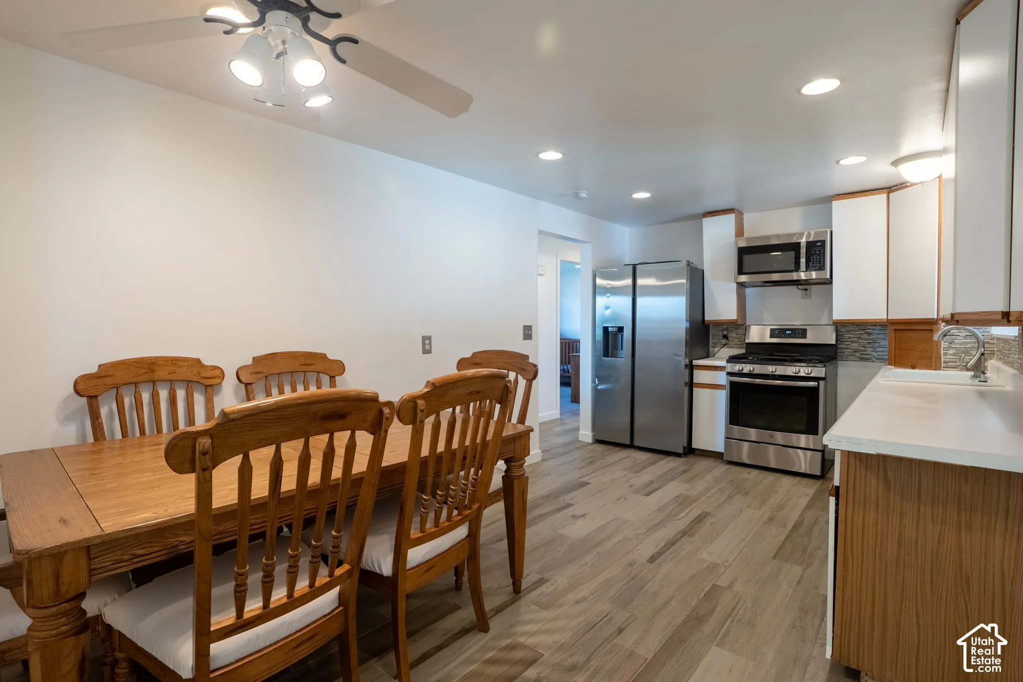 Kitchen and dining area featuring stainless steel appliances, white cabinetry, a tiled backsplash, wood-finish flooring, and recessed lighting