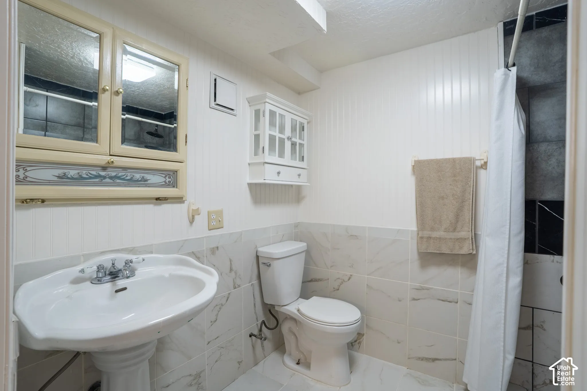 Pedestal sink with chrome fixtures, mirrored medicine cabinet, wall-mounted cabinet, toilet, and tiled shower area