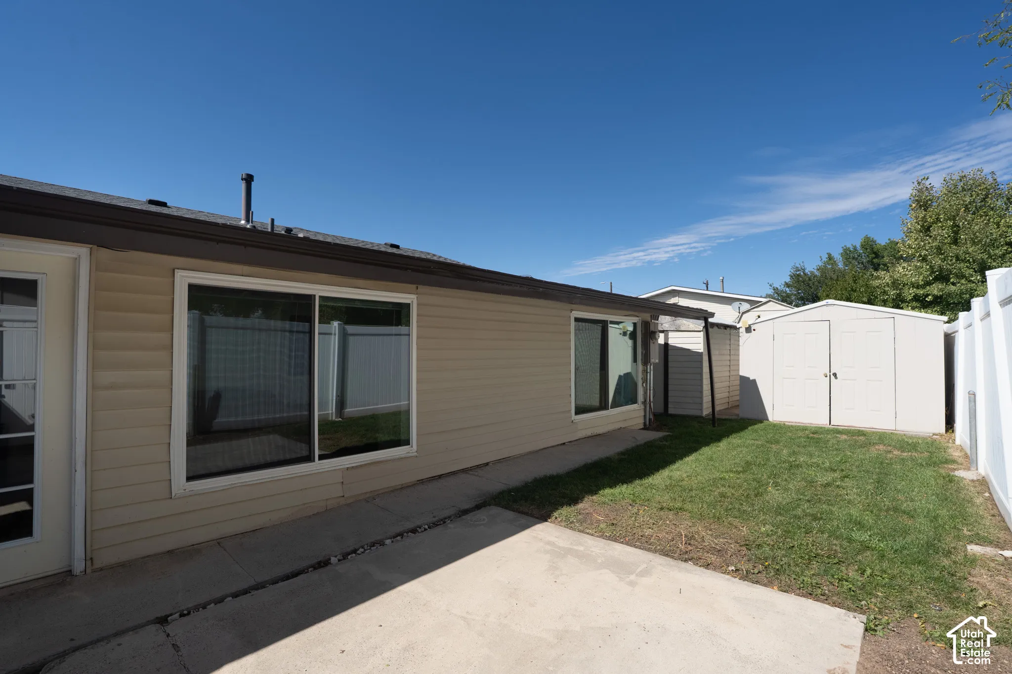 Backyard featuring a concrete patio, a grass area, and a white storage shed
