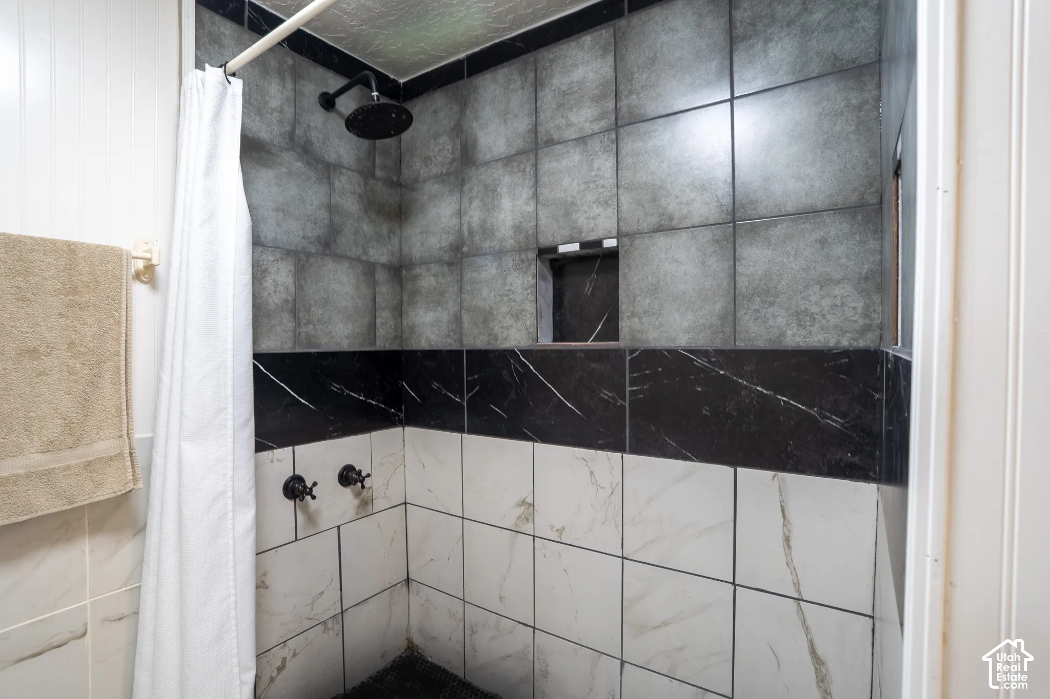 Tiled shower with a black rain showerhead, built-in niche, and dual-tone wall tiling