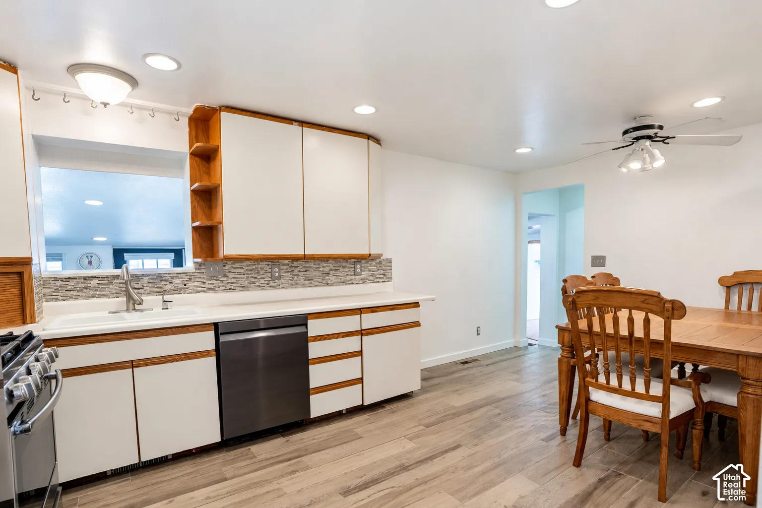 Kitchen featuring wood-finish flooring, white cabinetry with wood trim, stainless steel dishwasher, mosaic tile backsplash, and recessed lighting