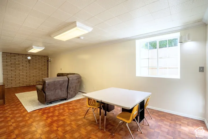 Room featuring wood-finish flooring, a light-colored brick accent wall, and a drop ceiling with integrated lighting