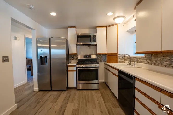 Kitchen featuring wood-finish flooring, white cabinetry with wood trim, stainless steel appliances, a mosaic tile backsplash, and light-toned countertops