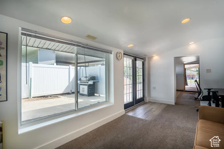 Recessed ceiling lighting, large picture window, white perimeter fencing, black French doors, and wood-finish flooring