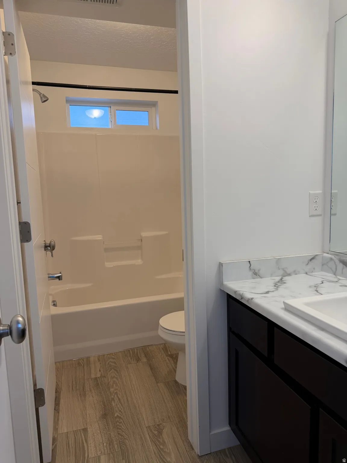 Bathroom featuring a white tub/shower combination, transom window, wood-finish flooring, dark wood-finish vanity, and a white countertop with integrated sink