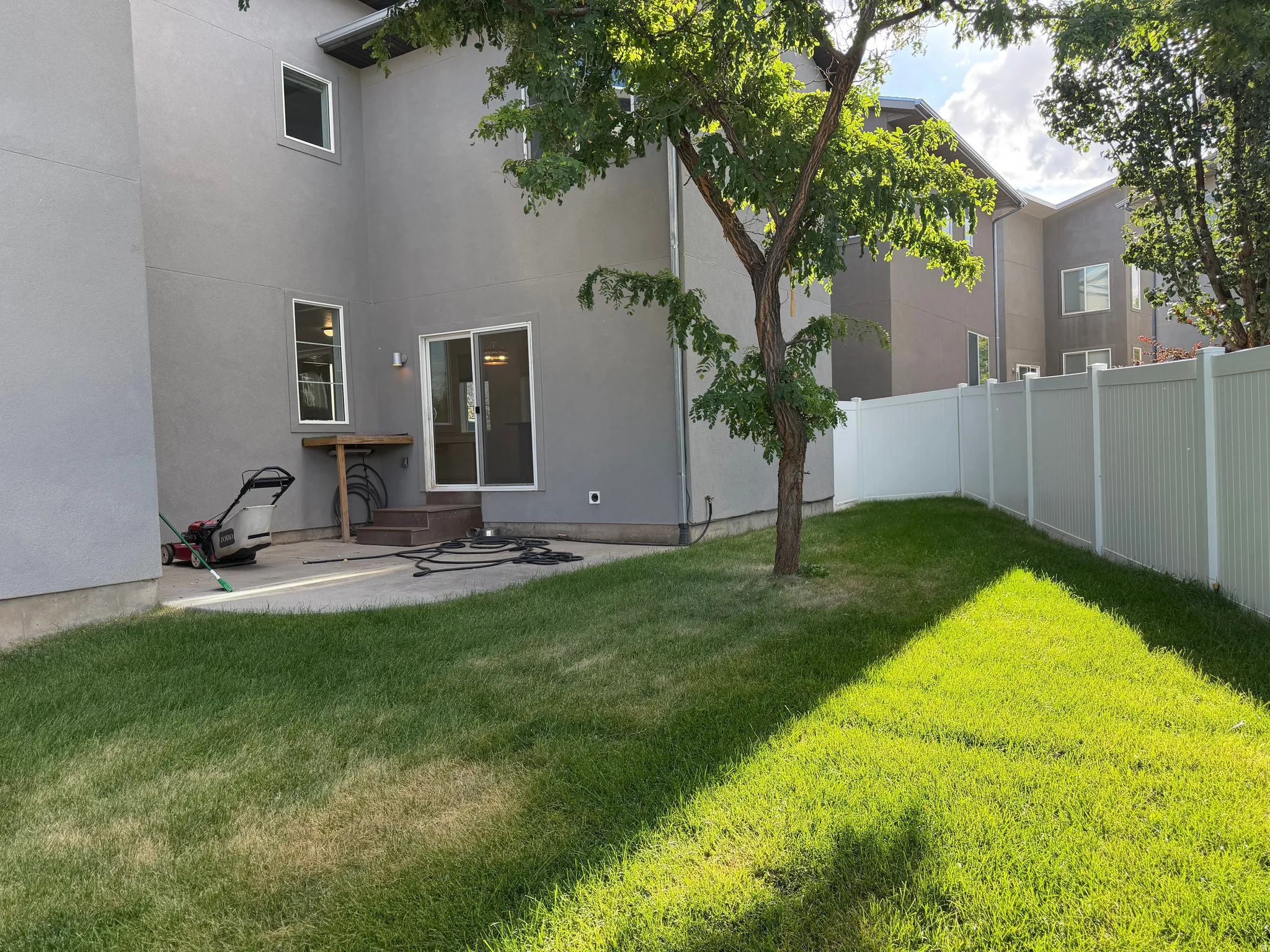 Private backyard with a manicured lawn, concrete patio, and white vinyl fencing