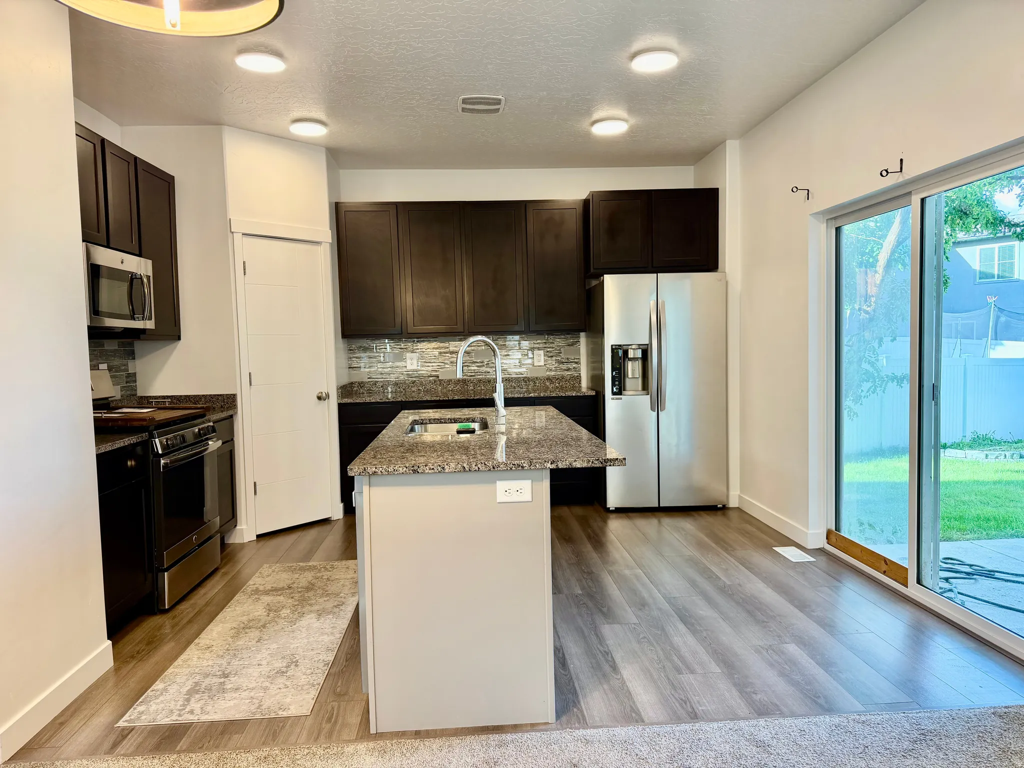 Kitchen featuring dark wood-finish cabinetry, stainless steel appliances, speckled stone countertops, and a full tile backsplash