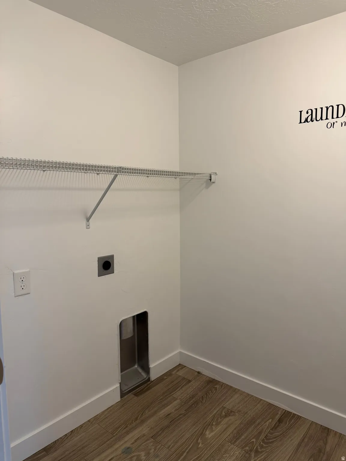 Wood-finish flooring with white baseboards, a wire shelving unit, and wall-mounted electrical outlets
