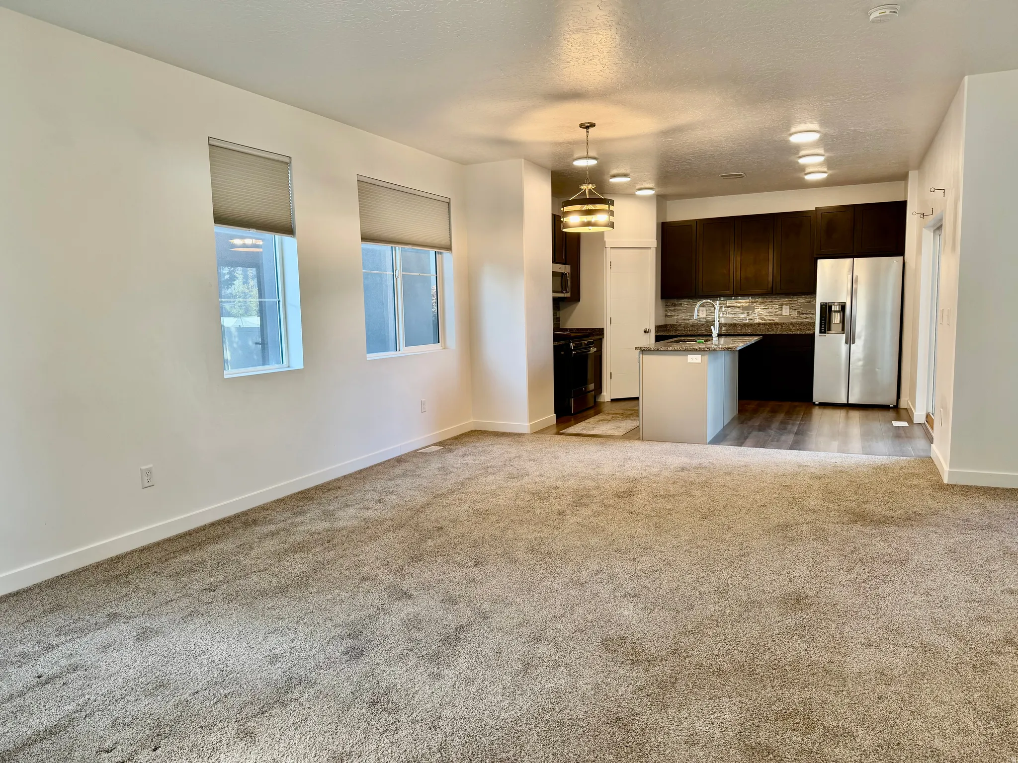 Open-concept living space featuring neutral carpet, recessed lighting, and a kitchen with dark wood cabinetry, stainless steel appliances, and an island with a sink