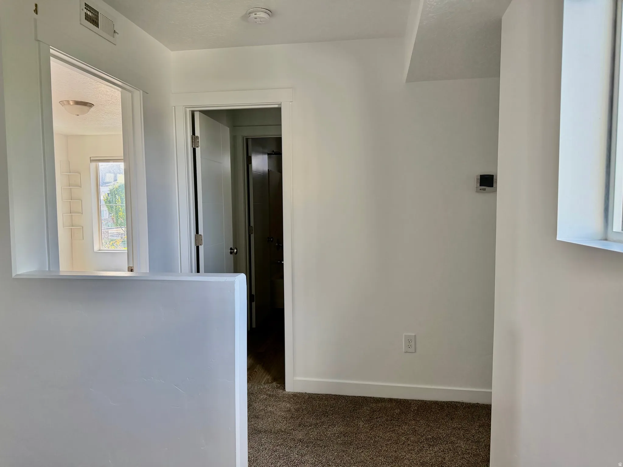 Interior hallway with neutral carpeting, white walls, and a pass-through opening