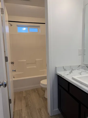 Bathroom featuring a white tub/shower combination, transom window, wood-finish flooring, dark wood-finish vanity, and a white countertop with integrated sink