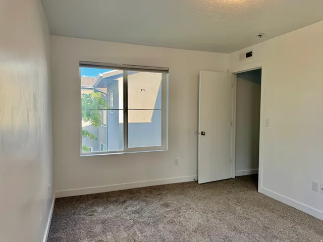 White painted walls, gray carpet flooring, and a single window with a white frame