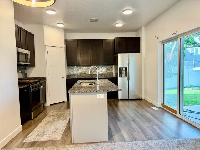 Kitchen featuring dark wood-finish cabinetry, stainless steel appliances, speckled stone countertops, and a full tile backsplash