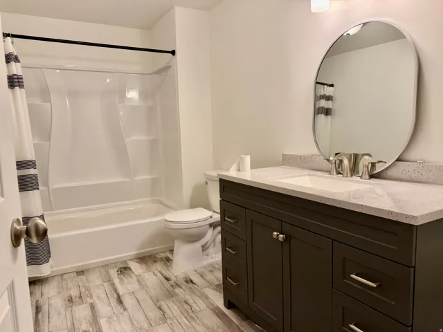 Bathroom featuring a tub/shower combination, dark wood-finish vanity, light-toned countertop, and an oval mirror