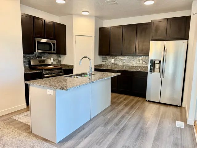 Contemporary kitchen featuring dark wood-finish cabinetry, stainless steel appliances, granite countertops, and a tiled backsplash