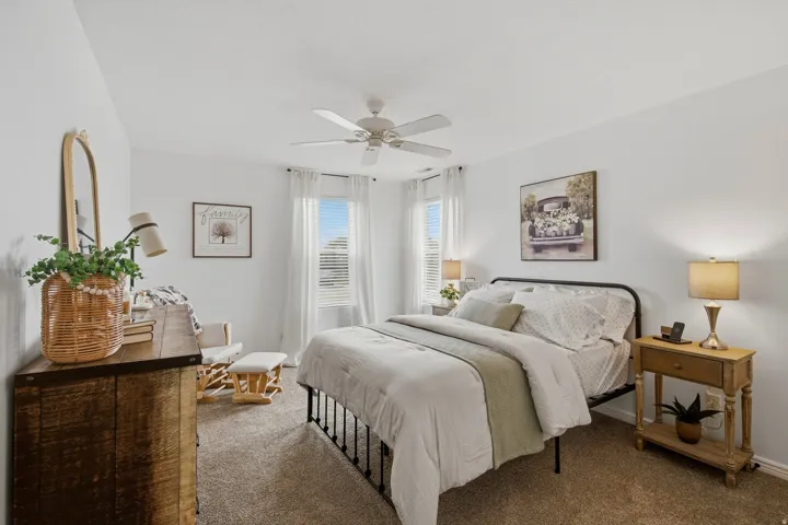 Carpeted bedroom with a ceiling fan, two windows with blinds, and white walls