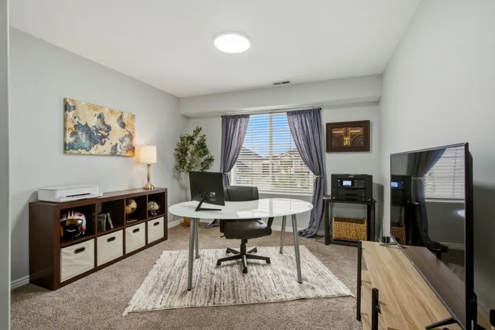 Recessed lighting, light gray wall color, carpeted flooring, large window with blinds, and a built-in shelving unit
