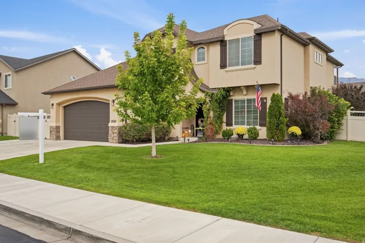 Stucco exterior with stone accents, arched garage door, shuttered windows, and mature landscaping