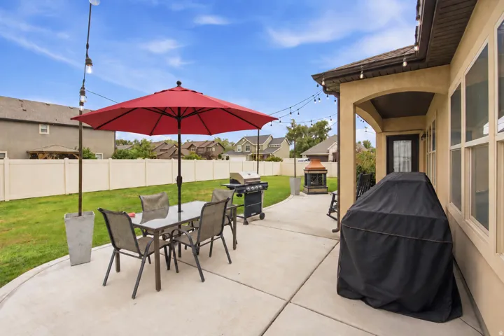 Expansive concrete patio with string lighting, covered porch entrance, and a fully fenced yard