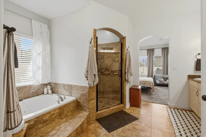 Built-in soaking tub, walk-in shower with glass enclosure, arched doorways, tiled flooring, and vanity with countertop