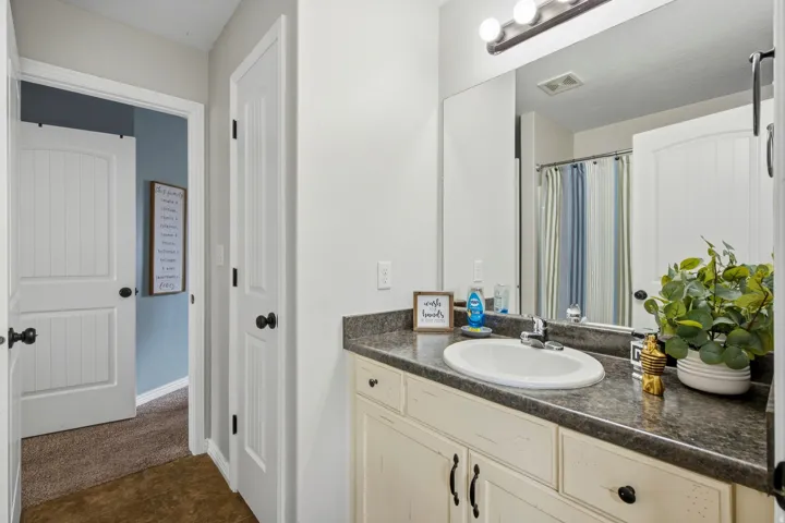 Vanity with a dark countertop and integrated sink, full-width mirror, and a three-light fixture