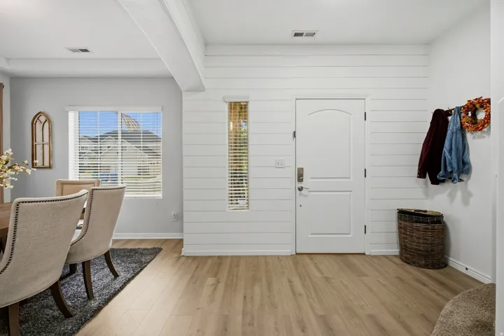 Wood-finish flooring, white shiplap accent wall, white interior door with arched paneling, and an elongated vertical window